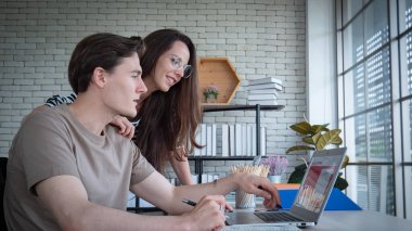 Ev ofisinden ya da ev konseptinden. Beyaz tenli bir erkek ve kadın evdeki ya da ofisteki masada dizüstü bilgisayarla ya da defterle oturuyor ve çalışıyor..