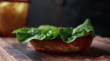 Şef ahşap tahtada biftek ve sebzeli hamburger pişiriyor.