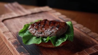 Şef ahşap tahtada biftek ve sebzeli hamburger pişiriyor.