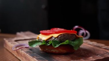 Şef ahşap tahtada biftek ve sebzeli hamburger pişiriyor.