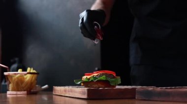 Şef ahşap tahtada biftek ve sebzeli hamburger pişiriyor.