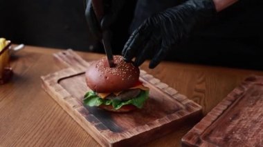 Şef ahşap tahtada biftek ve sebzeli hamburger pişiriyor.