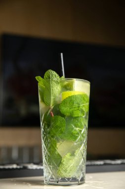 Bir bardak mojito kokteyli, yanında limon ve nane.