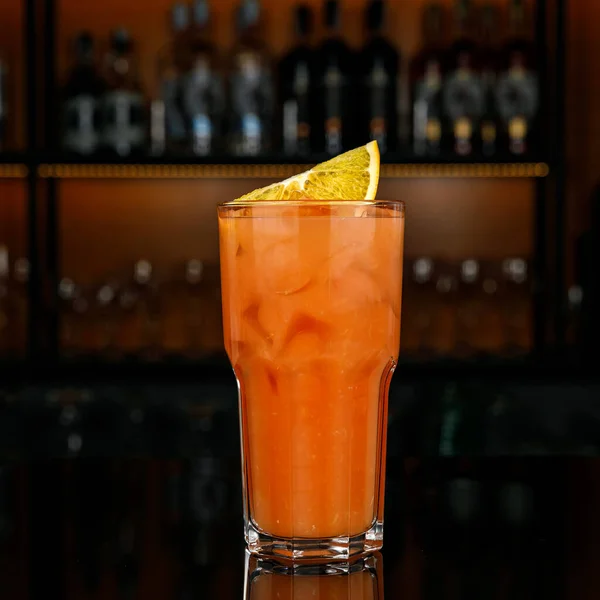 a glass of cocktail with a lemon and a straw on a bar counter