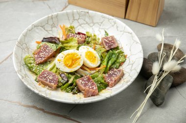 Ton balıklı salata, marul, otlar, yumurta, gri bir masada.