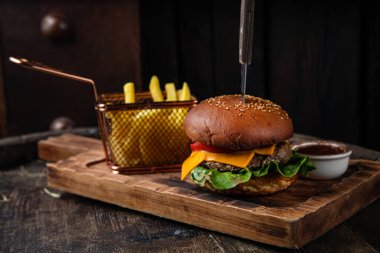 Biftek, peynir, marul, soğan ve salata ile ahşap arka planda ev yapımı hamburger.