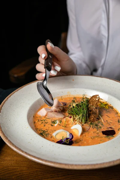 Beyaz tabakta çorba ve siyah arka planda bıçak olan bir kadın..