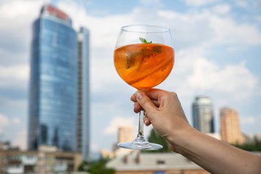 hand holding a glass of red cocktail with a lemon on the background of the sky
