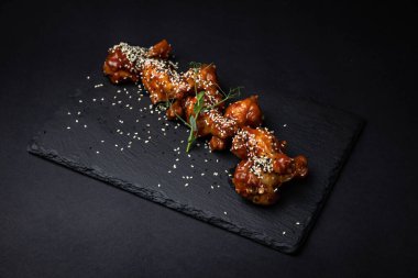 Izgara tavuk kanadı, soslu ve siyah arka planda baharatlı.