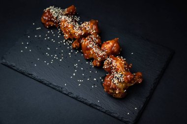 Susam tohumlu kızarmış tavuk kanatları ve siyah arka planda baharatlar.