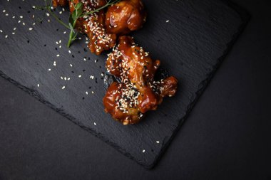 Susam tohumlu kızarmış tavuk kanatları ve siyah arka planda baharatlar.