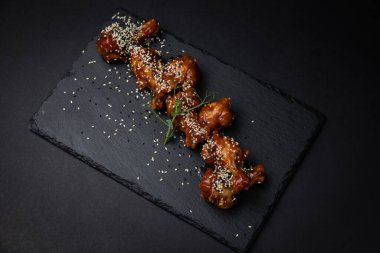 Susam tohumlu kızarmış tavuk kanatları ve siyah arka planda baharatlar.