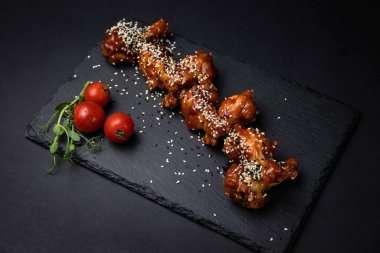 Susam tohumlu kızarmış tavuk kanatları ve siyah arka planda baharatlar.