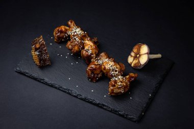 ızgara tavuk kanadı ve susam tohumları ve siyah arka planda baharatlar.