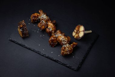 ızgara tavuk kanadı ve susam tohumları ve siyah arka planda baharatlar.