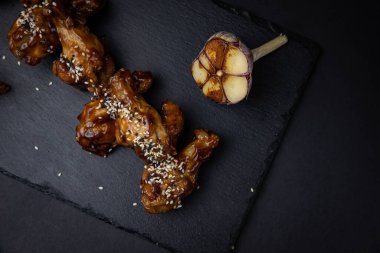 ızgara tavuk kanadı ve susam tohumları ve siyah arka planda baharatlar.