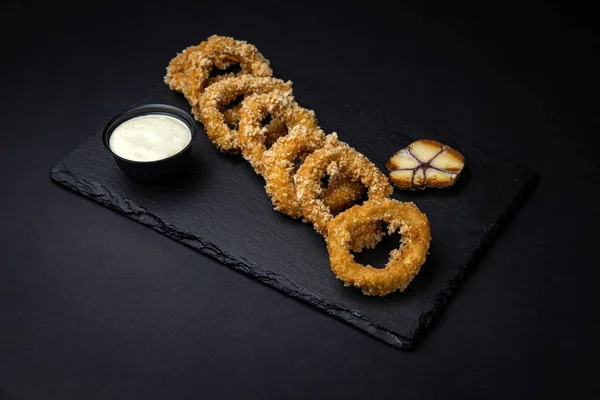 Koyu bir tahtada soslu ızgara kalamar halkaları.