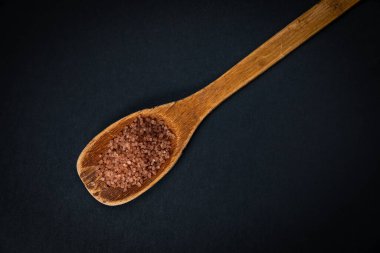 wooden spoon with a scoop of salt on a black background