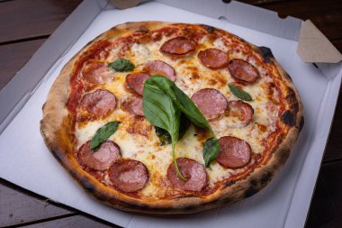 Ev yapımı Pepperoni, fesleğenli Salam Pizza, domates, tahta masa üzerine peynir. yemeye hazır