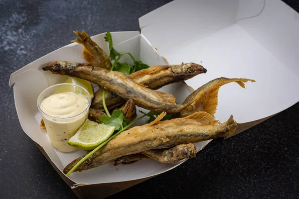 fried fish with vegetables and sauce on a disposable cardboard plate