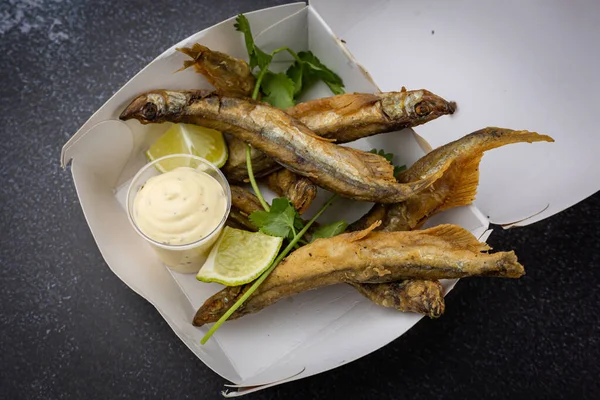 fried fish with vegetables and sauce on a disposable cardboard plate