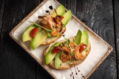 Siyah arka planda karides, avokado, domates ve fesleğenli sandviç..