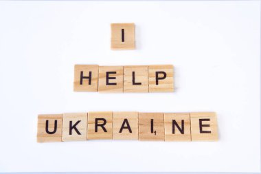 Ukrayna 'ya yardım ettiğim kelimelerin üst görünümü beyaz arka planda izole edilmiş ahşap karelerden oluşuyor. Mavi ve sarı kurdeleli Ukrayna bayrağıyla. Barış kavramı, Ukrayna 'da savaş, destek, savaş yok