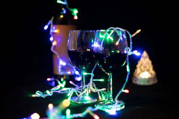 おもちゃのクリスマスツリーの輝くガーランドにある2つのワイングラス — ストック写真