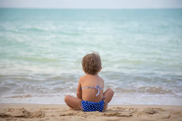 赤ちゃんの女の子は砂の上に座って 暖かい晴れた夏の日に海のビーチでおもちゃで遊んでいます 閉鎖だ バックビュー — ストック写真
