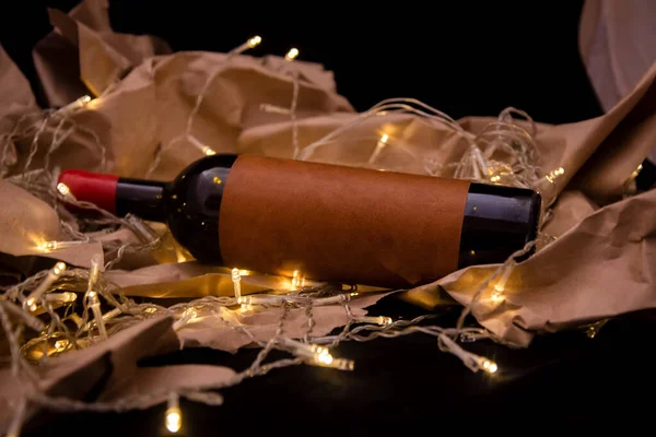 Μπουκάλι κρασί με λευκή ετικέτα βρίσκεται στο λαμπερό χρυσό γιρλάντα. μακιγιάρισμα χώρου αντιγραφής — Φωτογραφία Αρχείου