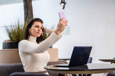 Akıllı telefondan arayan güzel bir kadın videosu dizüstü bilgisayarın başında oturuyor.