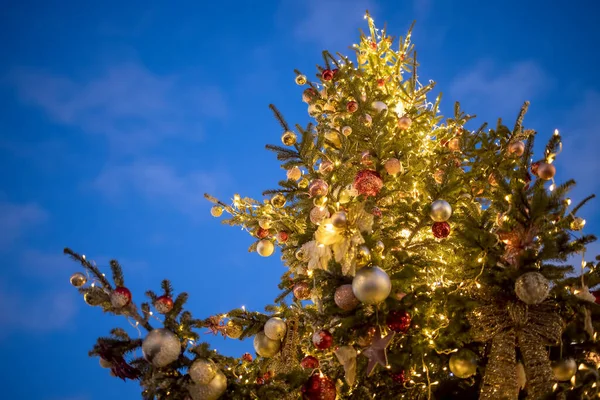 Nieuwjaar. onderaanzicht van prachtige hoge kerstboom versierd met ballen en lichtgevende bloemenslingers — Stockfoto