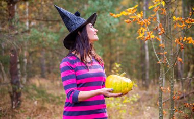 Genç cadı balkabağını sonbahar ormanında tutuyor.