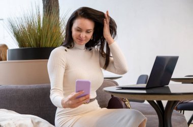 Akıllı telefondan arayan güzel bir kadın videosu dizüstü bilgisayarın başında oturuyor.