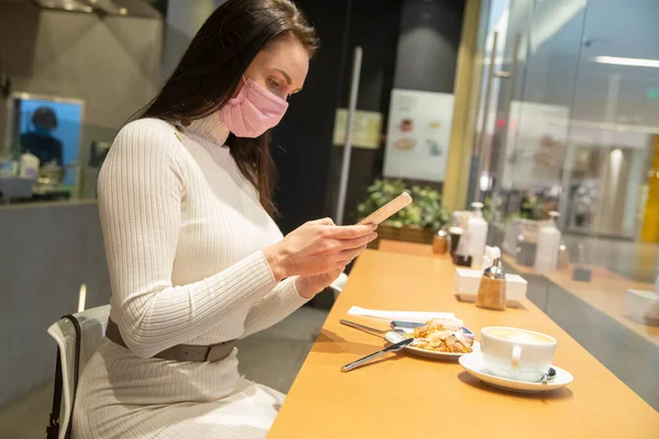 Mujer con máscara usando teléfono inteligente en la cafetería — Foto de Stock