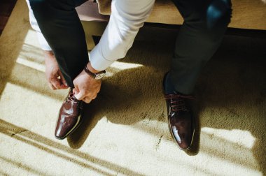 Takım elbiseli bir adam, damat, yakın plan ayakkabılarını giyer, bağcıklarını bağlar.
