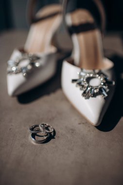 Gelin ayakkabısının arka planında değerli taşlar olan alyanslar.