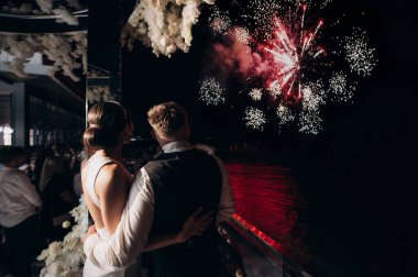 Yeni evliler şehrin üzerindeki gece havai fişeklerine bakıyorlar.