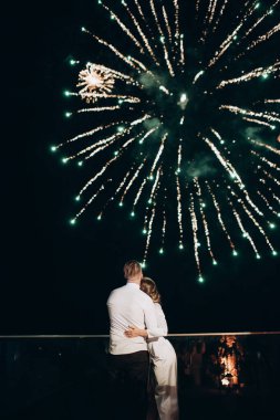 Yeni evliler şehrin üzerindeki gece havai fişeklerine bakıyorlar.