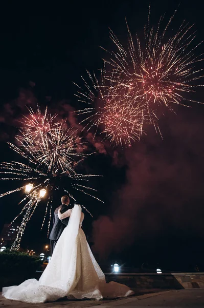 a couple of newlyweds look at the fireworks in the night sky over the city