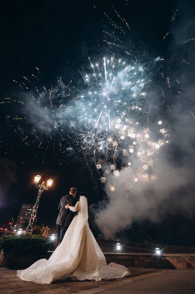 Yeni evliler şehrin üzerindeki gece havai fişeklerine bakıyorlar.