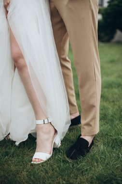 Yeni evliler çimlerin üzerinde durur, bacakları yakındır.