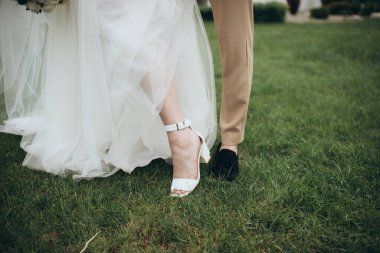 Yeni evliler çimlerin üzerinde durur, bacakları yakındır.