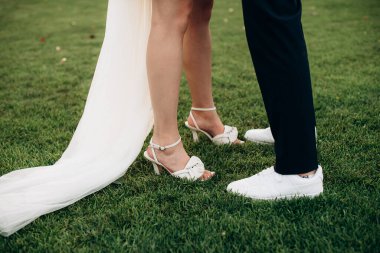 Yeni evliler çimlerin üzerinde durur, bacakları yakındır.