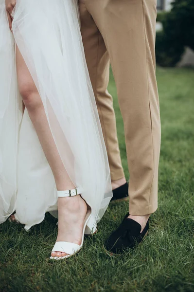 Yeni evliler çimlerin üzerinde durur, bacakları yakındır.