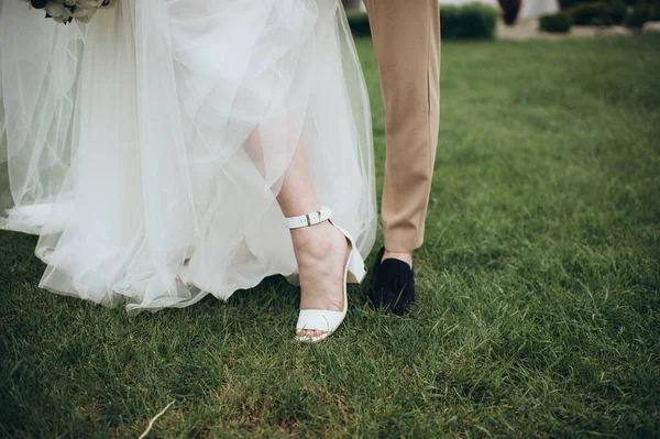 Yeni evliler çimlerin üzerinde durur, bacakları yakındır.