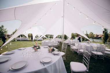 Çimlerin üzerinde beyaz bir çadırın altında ziyafet masası.