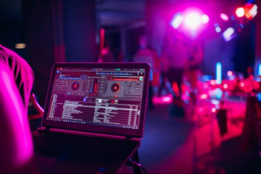 DJ bir bilgisayar klavyesi üzerinde çalışıyor. Gece lambası, DJ konsolu, disko ekipmanları.