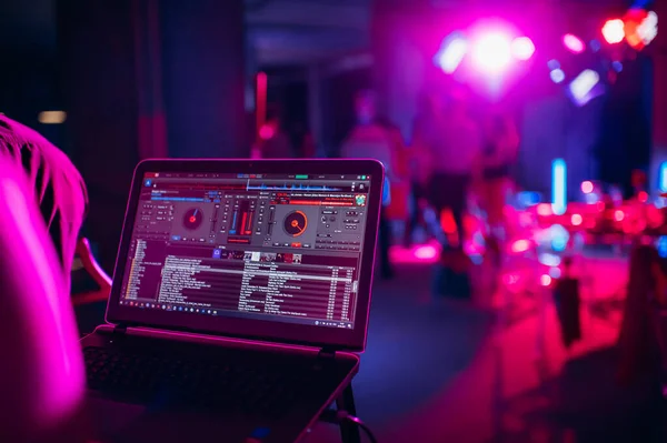 DJ bir bilgisayar klavyesi üzerinde çalışıyor. Gece lambası, DJ konsolu, disko ekipmanları.