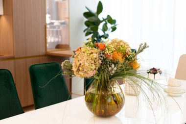 Küresel cam bir vazo içinde bir buket çiçek olan beyaz bir masa üzerinde modern tasarımcı iç mimarisi. Yumuşak seçici odak, sanatsal ses.